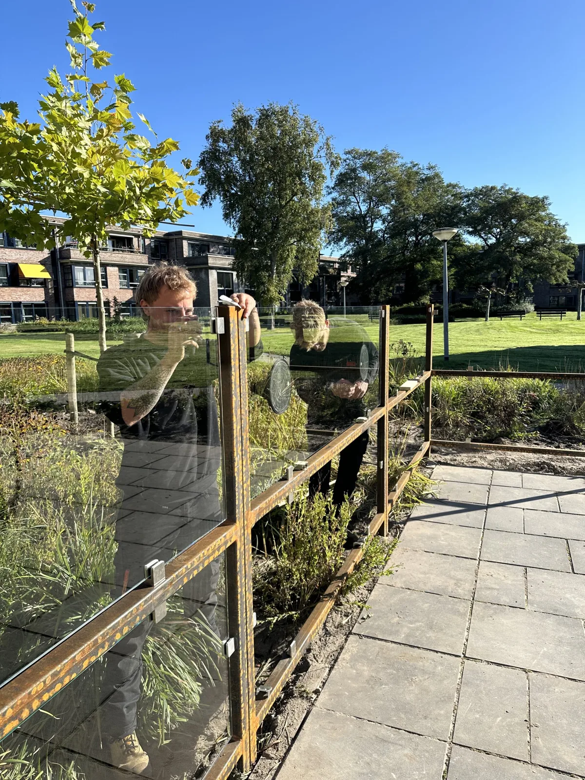 Glazen windscherm met stalen frame langs een tuinpad